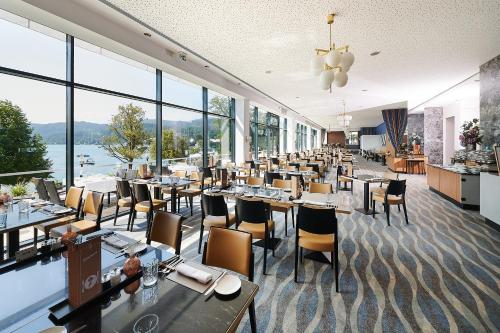 una sala da pranzo con tavoli, sedie e finestre di Parkhotel Pörtschach - Das Hotelresort mit Insellage am Wörthersee a Pörtschach am Wörthersee