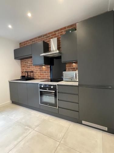 a kitchen with gray cabinets and a brick wall at Modern Luxury Escape Suite In The Heart of Urmston Town Centre in Urmston