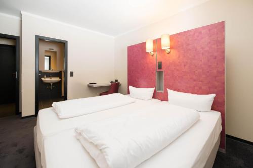 a bedroom with two white beds and a red wall at Hotel Topas Frankfurt City in Frankfurt/Main