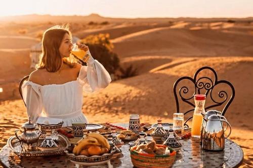 Eine Frau sitzt an einem Tisch in der Wüste und isst Essen. in der Unterkunft luxury desert night camp in Merzouga