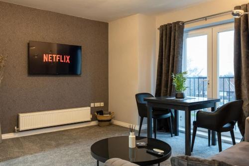 a living room with a table and a tv on the wall at SandyCroft- Secure gated Parking & Close To Airport in Wythenshawe