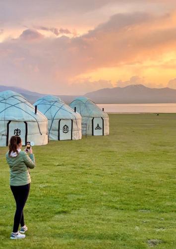 a woman taking a picture of a group of tents at Yurt Camp Ali-Nur, Lake Song-Kul , Kyrgyzstan, Юрточный лагерь Али Нур, на берегу озера Сон Кол in Naryn