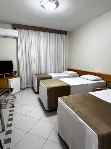 a hotel room with three beds and a flat screen tv at Hotel Nacional Inn Cuiabá in Cuiabá