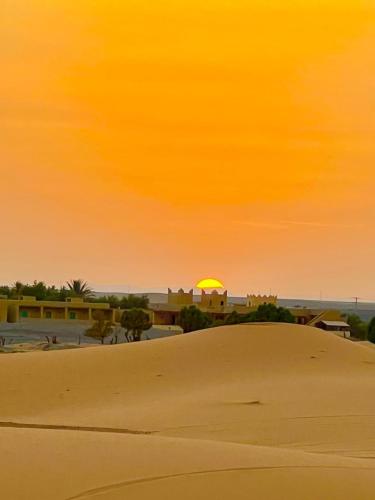 a sunset over the desert with a sand mound at Desert camp camel & sandboarding in Merzouga