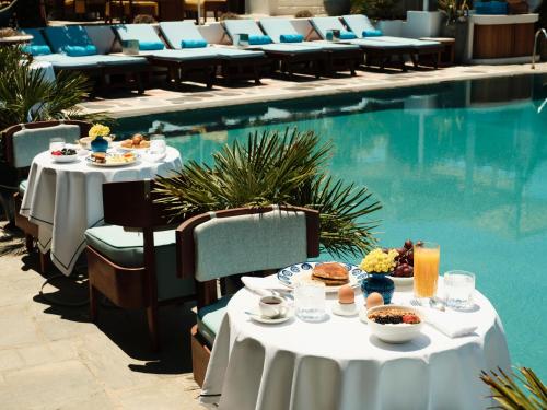 a table with food on it next to a swimming pool at Belvedere Mykonos - Main Hotel - The Leading Hotels of the World in Mýkonos City
