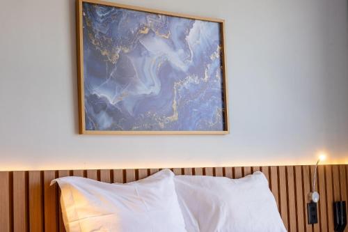 a painting above a bed with white pillows at Alta Garden Housi João Pessoa by Carpediem in João Pessoa