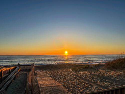 a sunset on the beach with the sun setting over the ocean at K1410 Loggerhead Landing - Oceanside Condo Just Steps to the Beach! in Croatan Shores