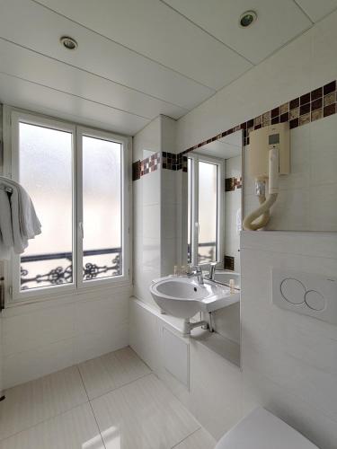 ein weißes Badezimmer mit Waschbecken und Spiegel in der Unterkunft Hotel Havane Opera in Paris