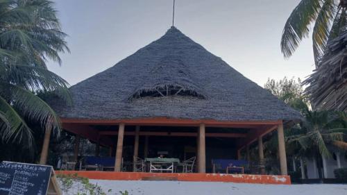 a restaurant with a straw roof with a table at Beach Front Bungalow in Jambiani