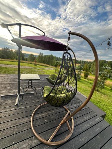 a swing with an umbrella and a table on a deck at Melnā kalna kamene in Vestiena