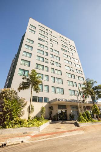 a tall white building with palm trees in front of it at IT Itabira Hotel in Itabira