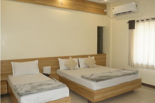 a bedroom with two beds with white sheets and a window at Hotel Radhika in Somnath