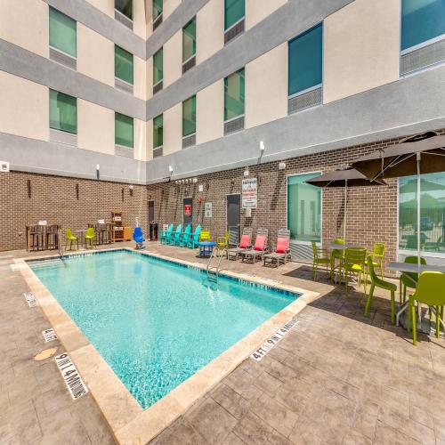 a swimming pool with chairs and tables and a building at Home2 Suites By Hilton Fort Worth Arlington West in Fort Worth
