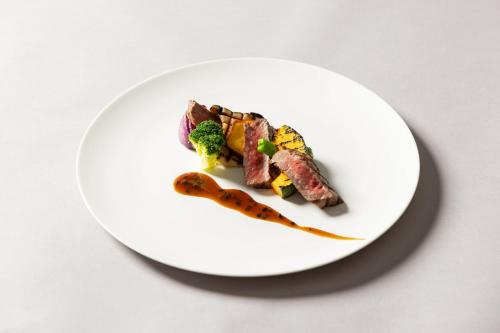 a white plate with meat and vegetables on a table at Hotel Indigo Nagasaki Glover Street by IHG in Nagasaki