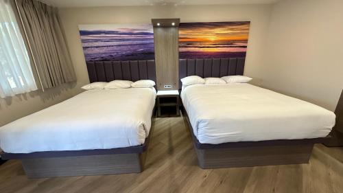 two beds in a room with a picture on the wall at Costa Mesa Inn - Newport Beach Area in Costa Mesa