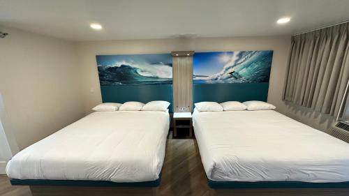 two beds in a room with a painting on the wall at Costa Mesa Inn - Newport Beach Area in Costa Mesa