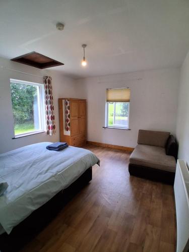 a bedroom with a bed and a chair and two windows at Ciaran's cottage in Donore