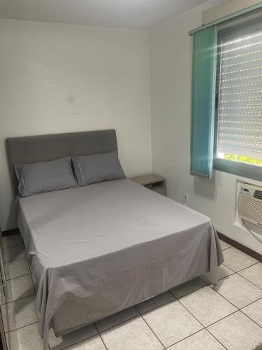 a bed in a white room with a window at AP prox Unisinos-Trem com 2 AC e 2 smart TV in São Leopoldo
