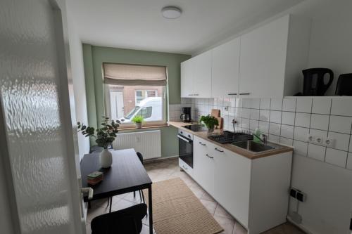 une cuisine avec des armoires blanches, une table et une fenêtre dans l'établissement L21-Apartment Geilenkirchen OT Teveren, 3 Zimmer, 6 Betten, Standardisierte Ausstattung, ideal für Reisende, Pendler, Familien, à Geilenkirchen