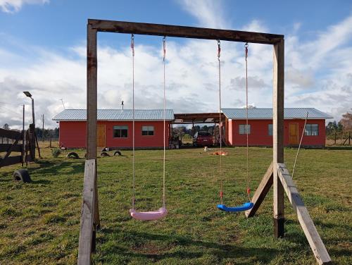 a playground with swings in a field with a building at Cabaña Vista Hermosa in Traitraico