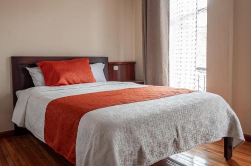 a bedroom with a bed with an orange pillow and a window at Hotel Campanario in Cuenca
