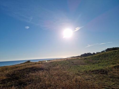 a sun is shining over a grassy hill next to the ocean at 4 person holiday home in Allingåbro-By Traum in Allingåbro