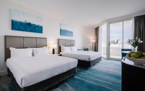 a hotel room with two beds and a balcony at Rendezvous Hotel Perth Scarborough in Perth