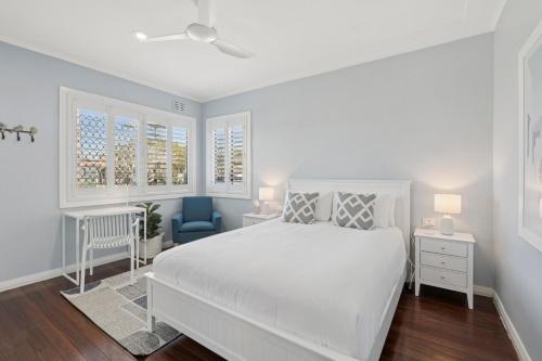 a white bedroom with a bed and a blue chair at Endless Summer Sawtell, Pool, Sleeps 6, Fun in Sawtell