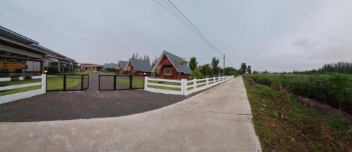 a driveway with a white fence and a small house at บ้านน้ำผึ้งโฮมสเตย์ in Suan Phung