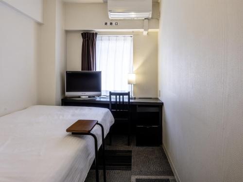 a hotel room with a bed and a desk with a television at KOKO HOTEL Yokohama Tsurumi in Yokohama