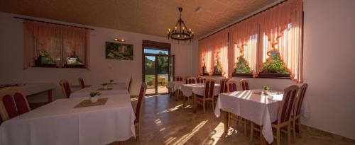 uma sala de jantar com mesas e cadeiras brancas e janelas em Plitvice Rooms em Smoljanac
