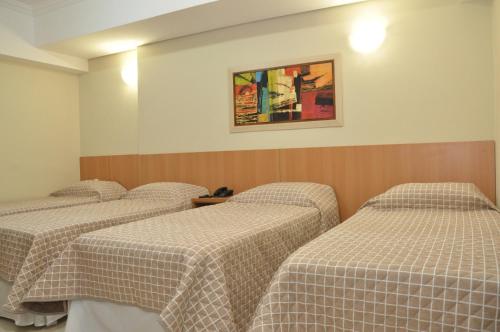 three beds in a room with checkered sheets at Lotus Hotel - à 6 km do Santuário de Aparecida-SP in Guaratinguetá