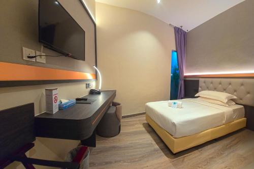 a hotel room with a bed and a desk with a television at Abell Hotel in Kuching