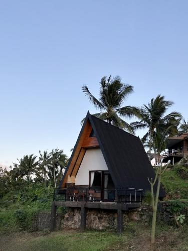 a house with a black roof and some palm trees at Bukit Langit Campventure in Glagah