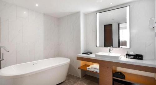 a bathroom with a tub and a sink and a mirror at Hampton by Hilton Zhuhai Doumen in Zhuhai