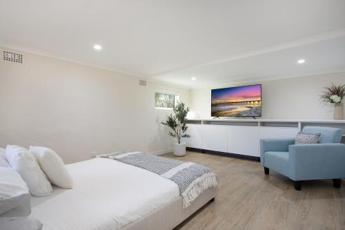 a white bedroom with a bed and a blue chair at Idyllic 4-Bed Home With Alfresco Area Near Beach in Deewhy