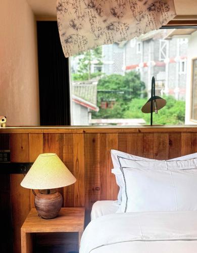 a bedroom with a bed with a lamp and a window at M Country Road 山行野奢影院温泉民宿 in Dujiangyan