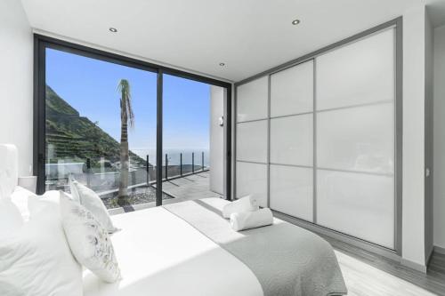 ein Schlafzimmer mit einem großen weißen Bett und einem großen Fenster in der Unterkunft Villa Calheta Charm by Villa Plus in Arco da Calheta