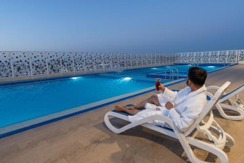 a man sitting in a chair next to a swimming pool at Dancenter Jeddah Near King Fahd's Fountain in Jeddah