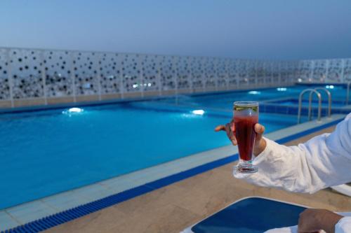 a person holding a drink in front of a swimming pool at Dancenter Jeddah Near King Fahd's Fountain in Jeddah