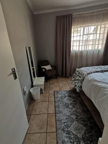 a bedroom with a bed and a chair and a window at J's Haven Self-Catering in Kimberley