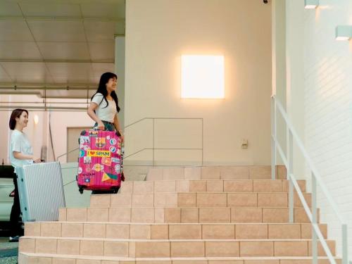 a woman walking up some stairs with a suitcase at HOTEL minimumms女性専用カプセルホテルWomen only hotel in Naha