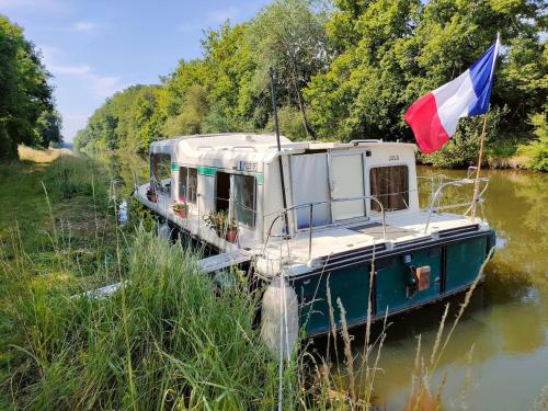 ein Boot mit einer Flagge am Ufer eines Flusses in der Unterkunft nuitée insolite aux berges d'un canal tranquille 