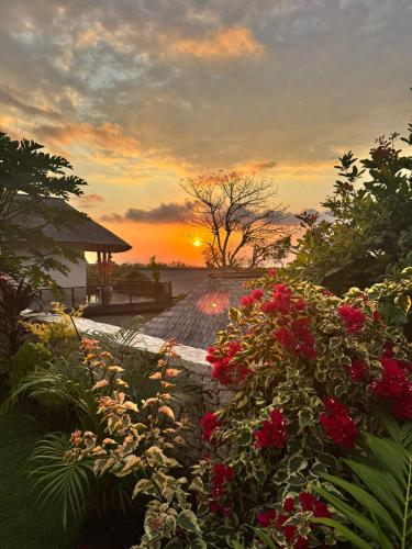 a sunset over a garden with red flowers at Penida View Village - Infinity pool & Volcano View in Nusa Penida