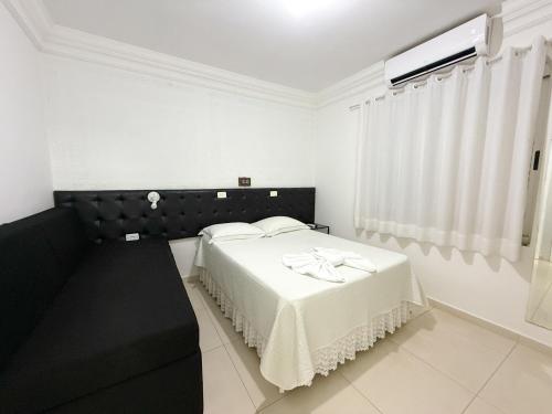 a white bedroom with a bed and a window at Grande Hotel in Paranavaí