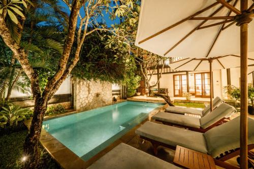 a swimming pool with chairs and an umbrella at Jimbaran Beach Villas by Nakula in Jimbaran