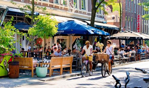 two women riding bikes down a street in a city at Haven Hotel Rotterdam, Curio Collection by Hilton in Rotterdam