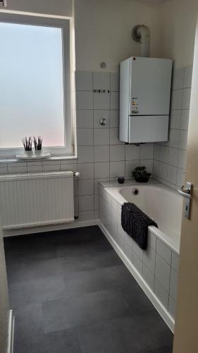 a white tiled bathroom with a tub and a window at Ferienwohnung Gästehaus Bauer 2 in Heiligenhaus