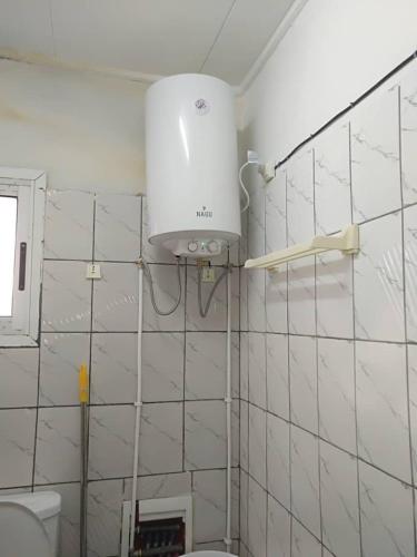 a white tiled bathroom with a toilet and a light at chambre meublé Douala bonapriso Cameroun, eau chaude, clim, gardien, wifi haut débit in Douala