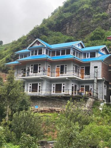 a large house with a blue roof on a hill at River Era by Naavagat in Jibhi